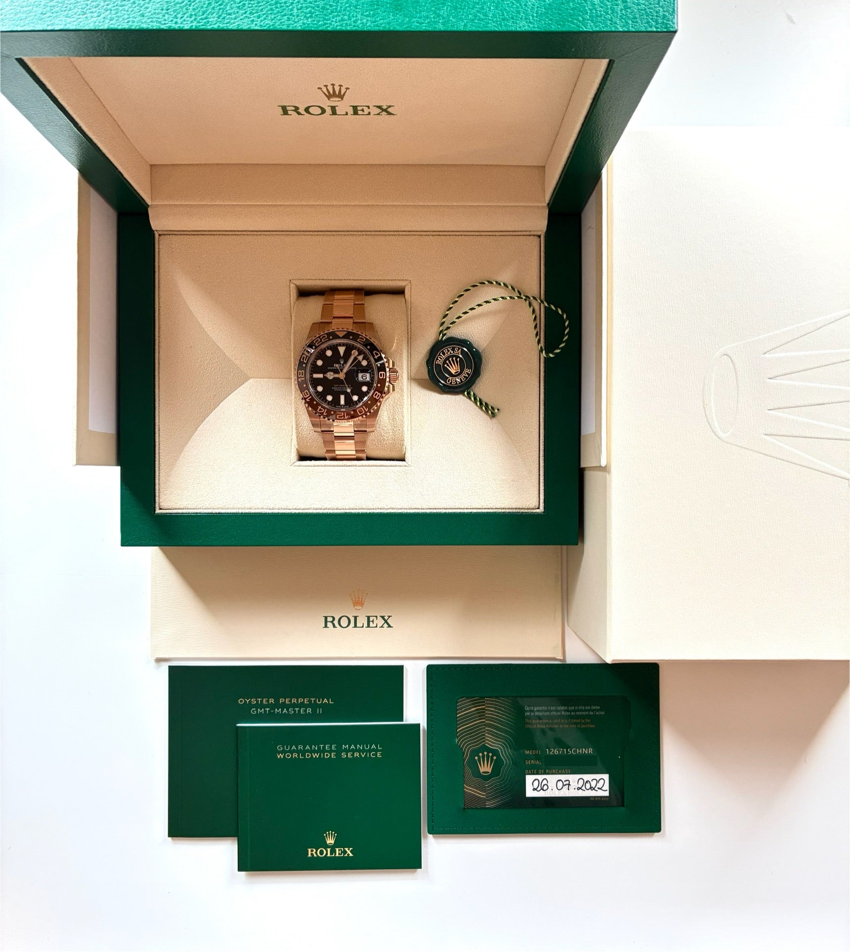 Eine Rolex GMT-Master II Roségold mit braunem Zifferblatt und Lunette in einer grünen Box mit Papieren