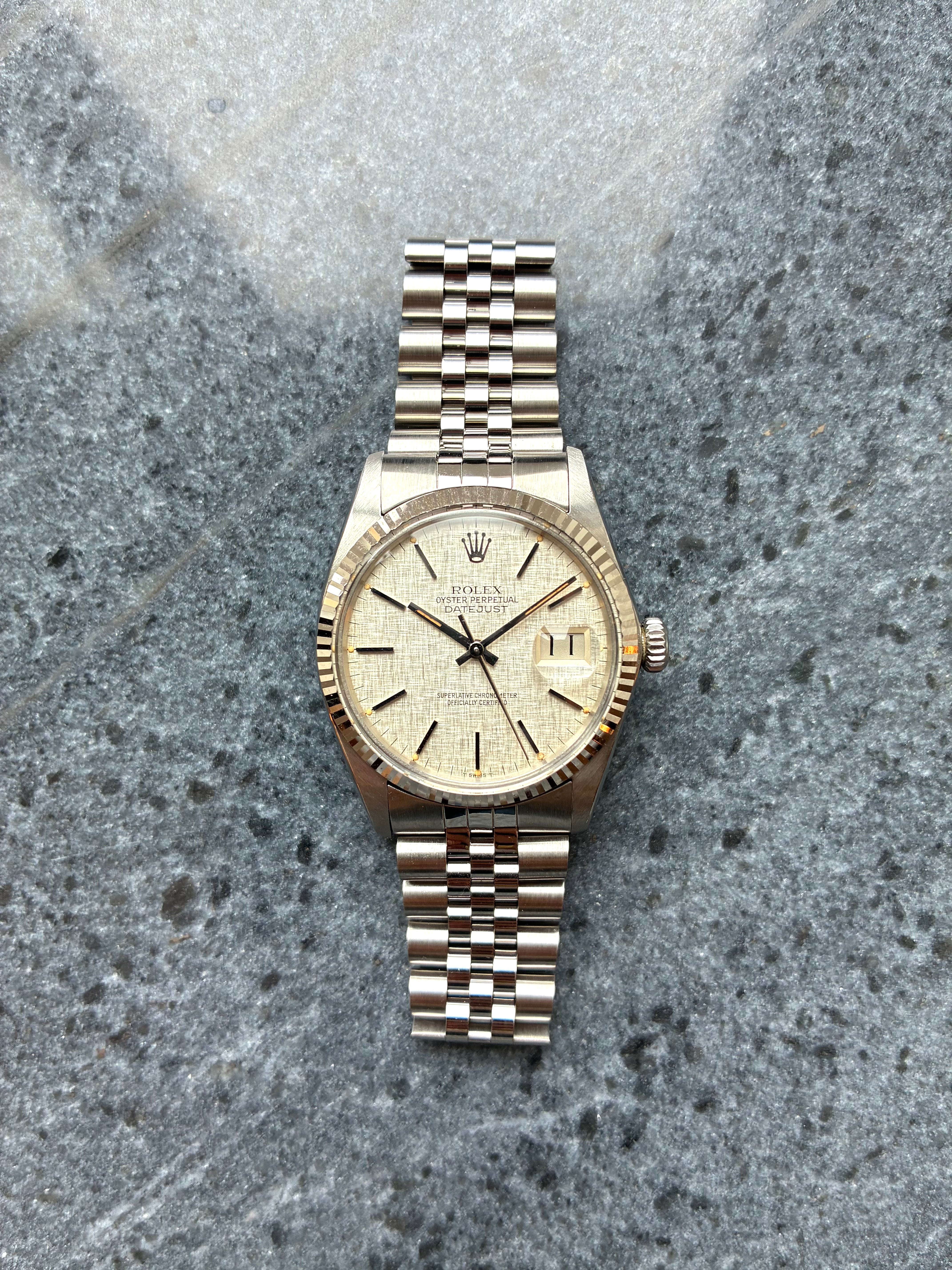Rolex Datejust 36mm Stahl mit silbernem Zifferblatt und Jubilee-Armband vor grauem Marmorhintergrund
