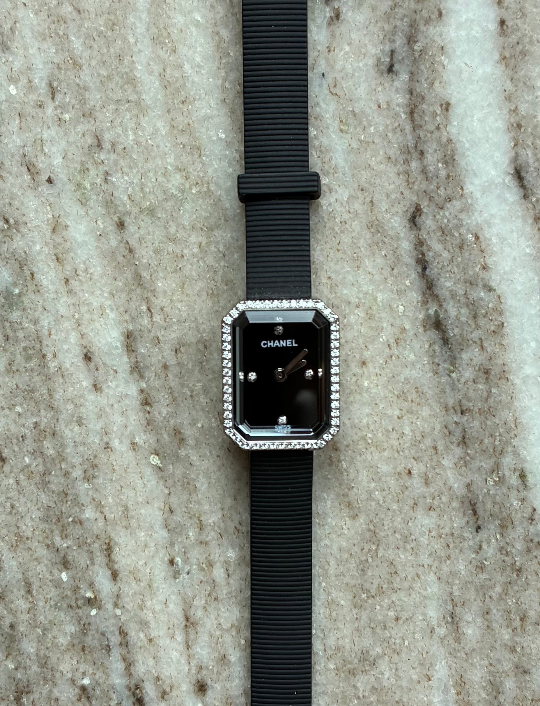 Chanel Premiere Damenuhr mit schwarzem Zifferblatt, 48 Diamanten auf der Lünette und schwarzem Armband auf Steinhintergrund