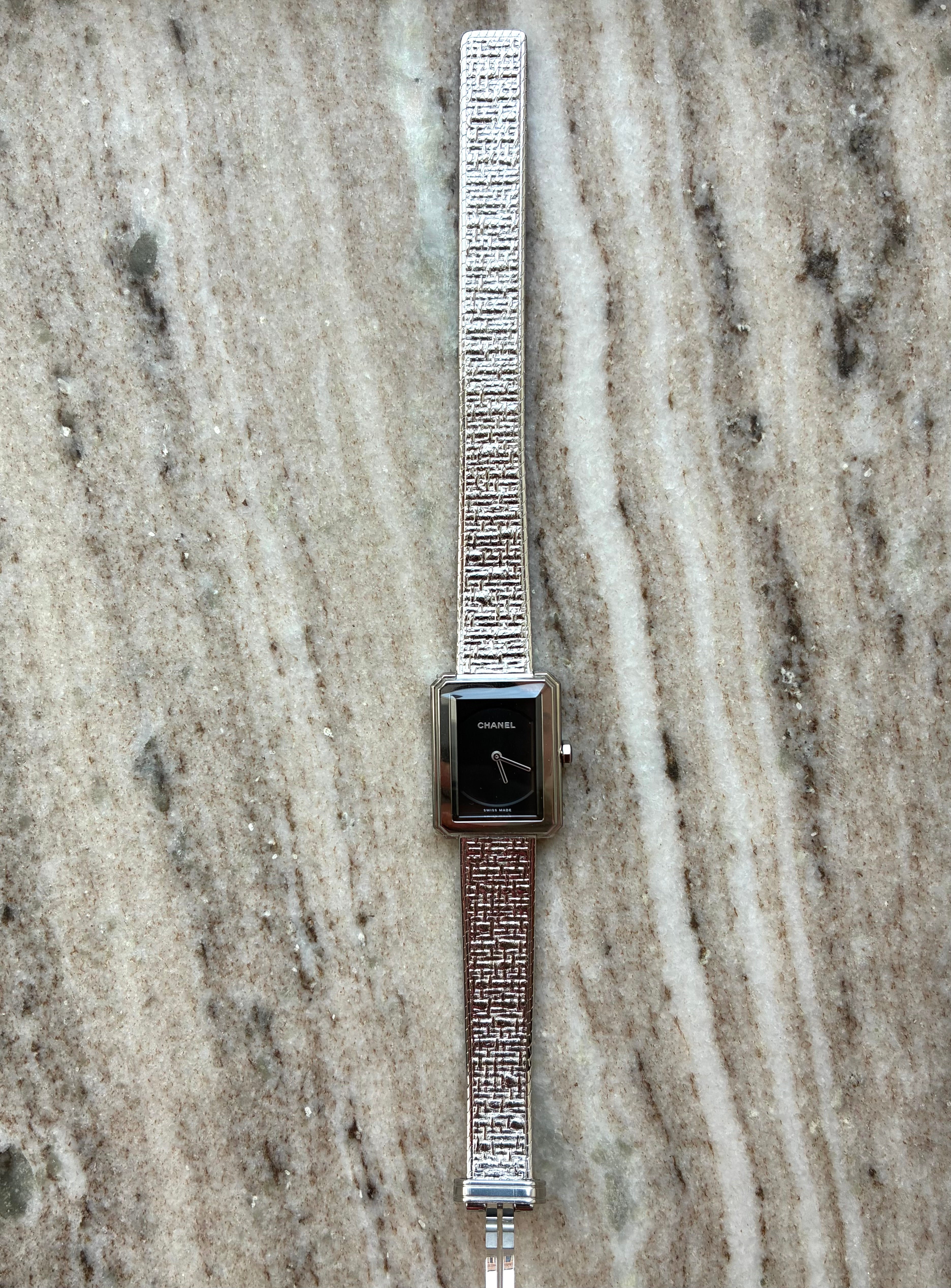Chanel Boyfriend Uhr mit schwarzem Zifferblatt und Edelstahlarmband auf Marmorhintergrund