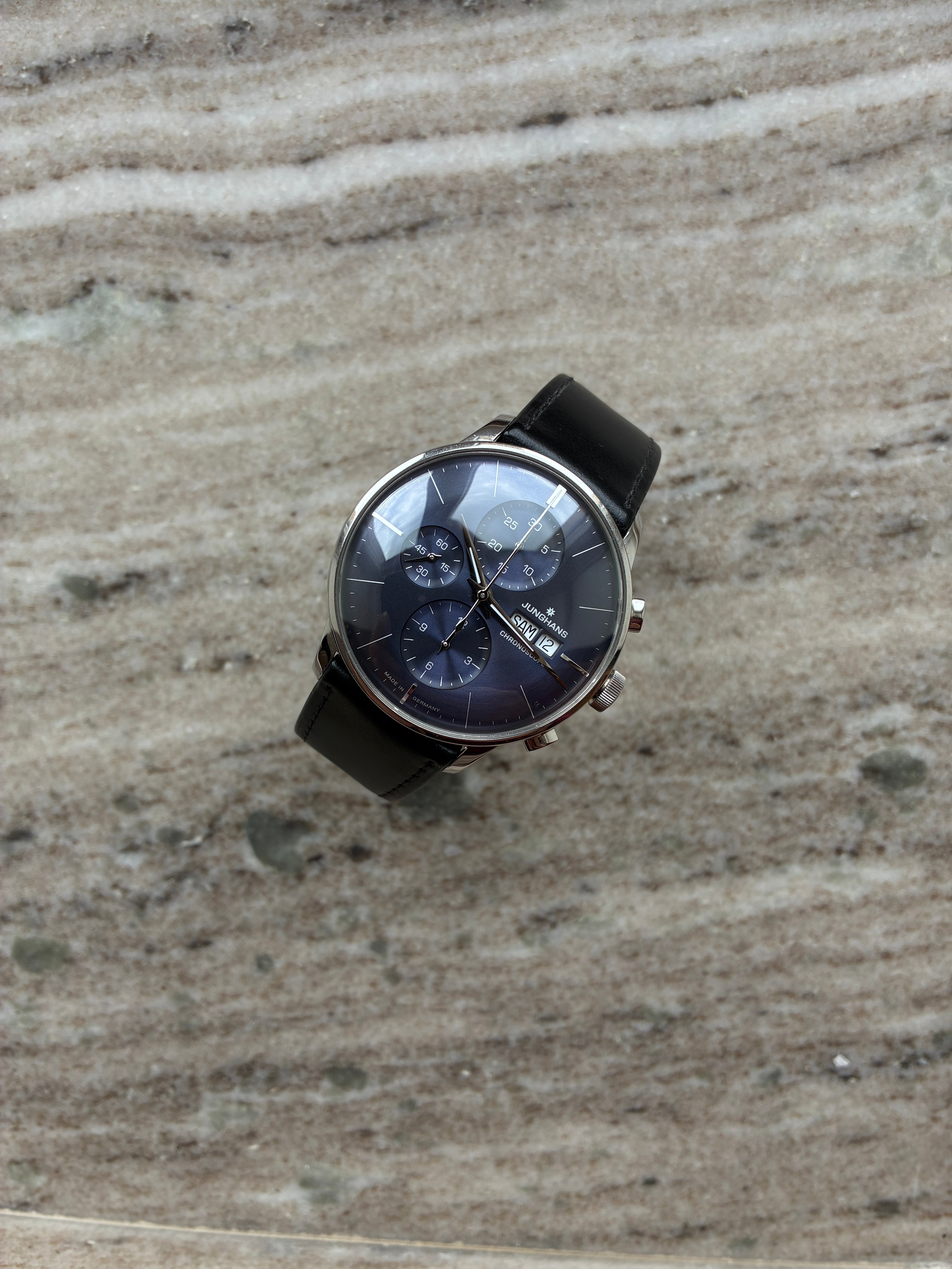 Junghans Meister Chronoscope mit schwarzem Lederarmband und blauem Zifferblatt auf strukturiertem Untergrund