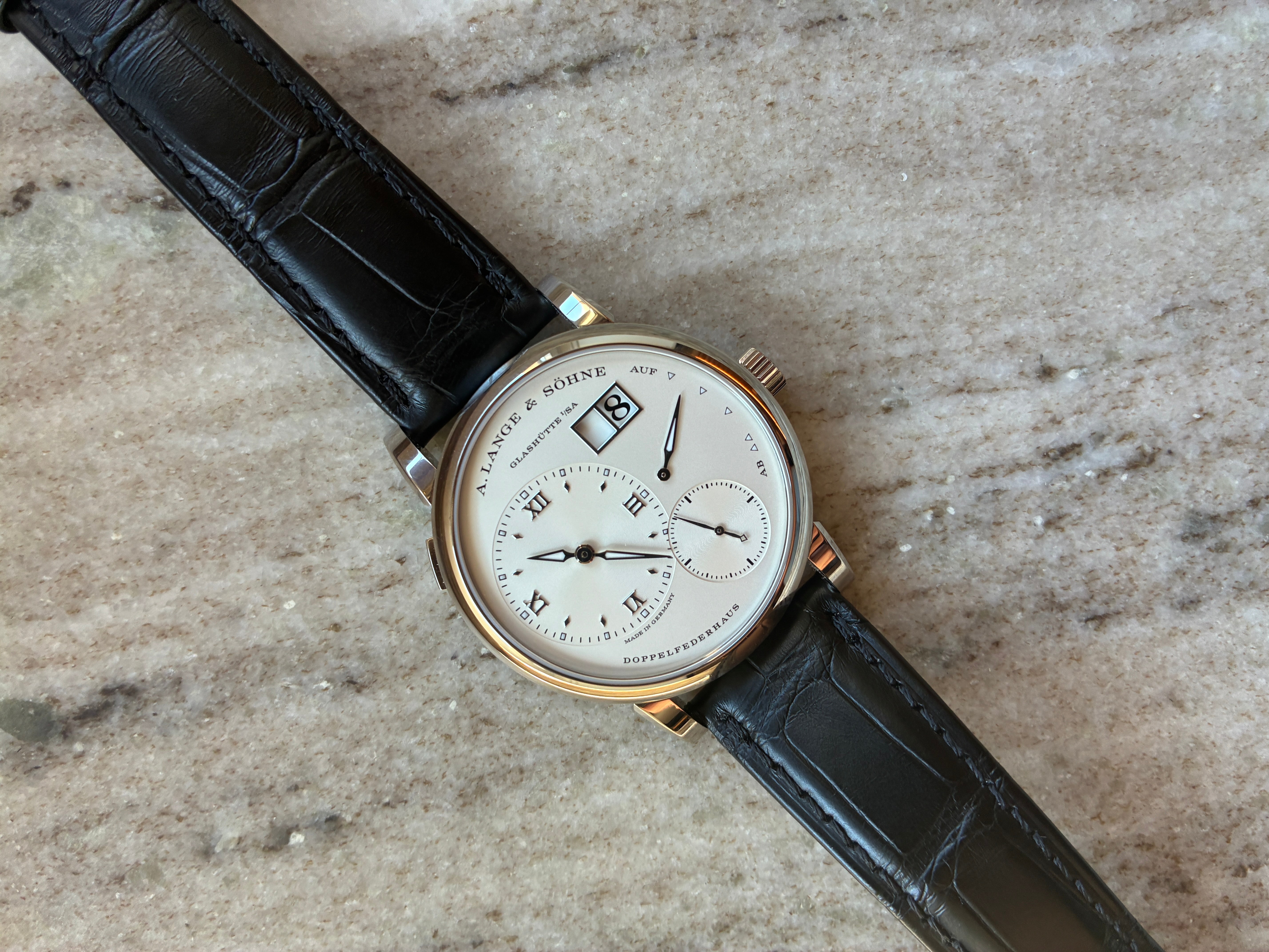 A. Lange & Söhne Lange 1 mit weißem Zifferblatt und schwarzem Lederarmband auf Steingrund