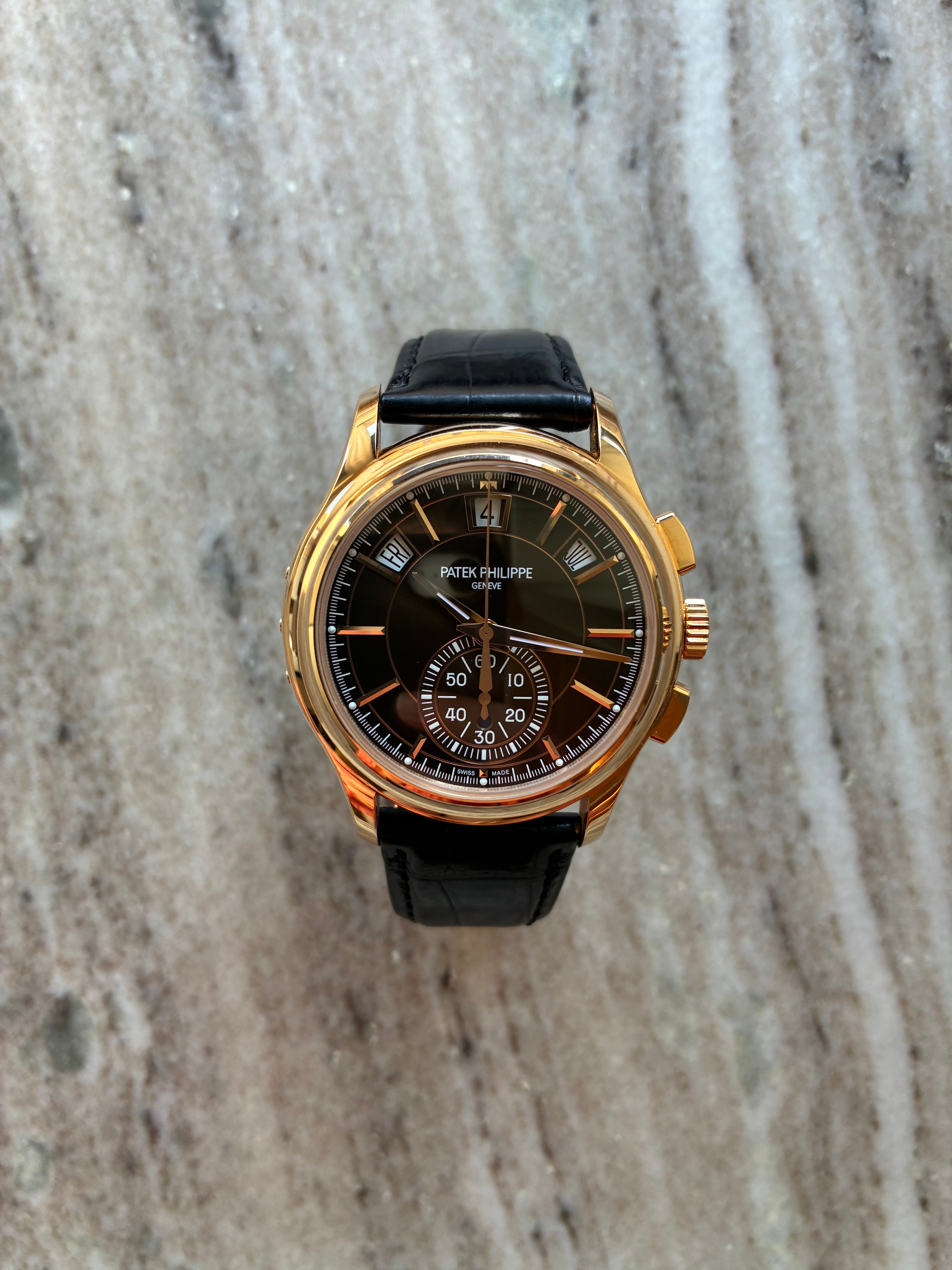 Patek Philippe Annual Calendar Chronograph Roségold mit schwarzem Zifferblatt und Lederarmband auf Marmorhintergrund