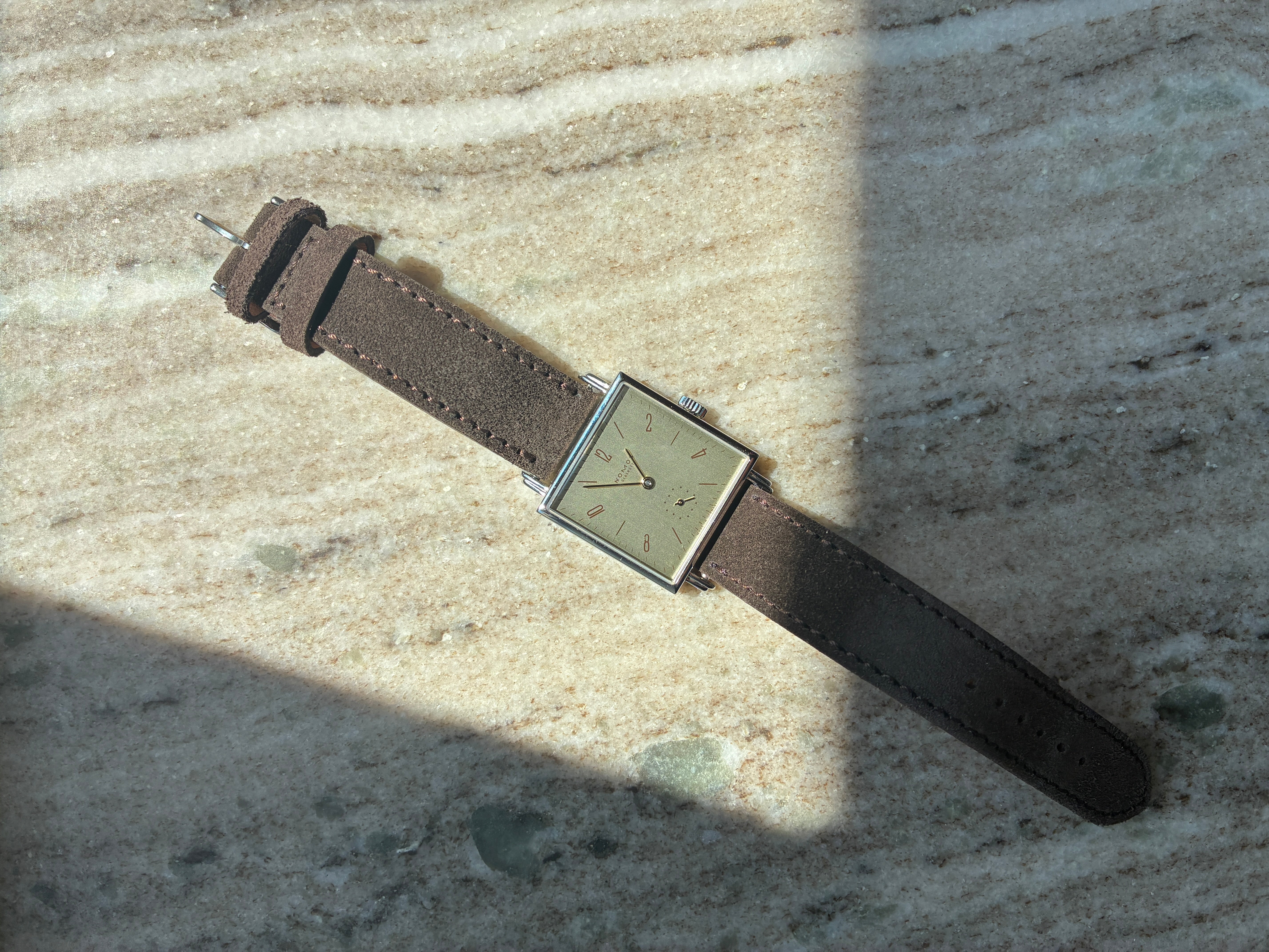 Nomos Tetra 27 Karat Like Unworn mit braunem Lederband auf Marmoruntergrund