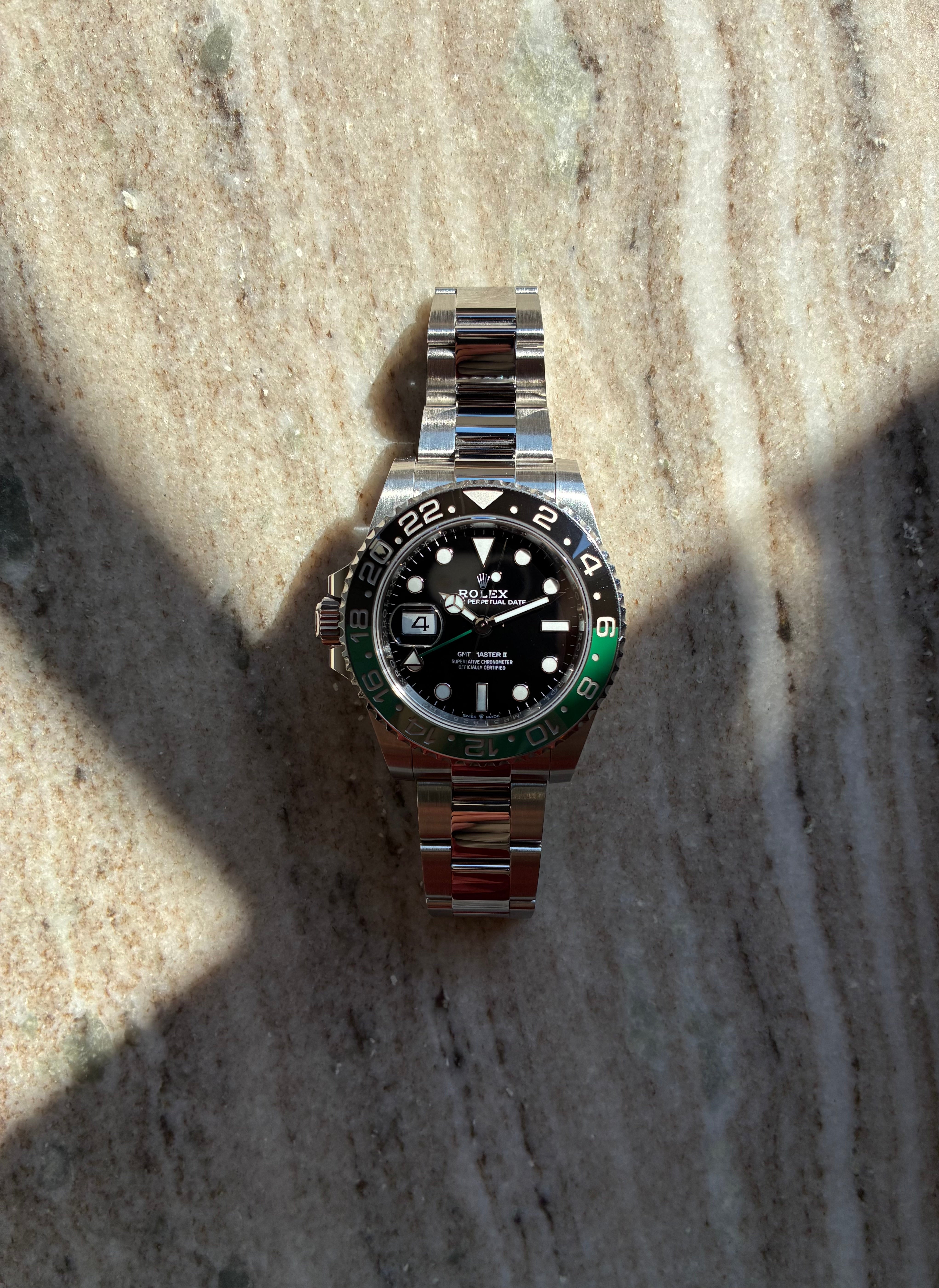 Eine neue Rolex GMT-Master II Lefthand (2023) aus Edelstahl mit schwarzem Zifferblatt und grüner Lünette liegt auf einem marmorierten Untergrund
