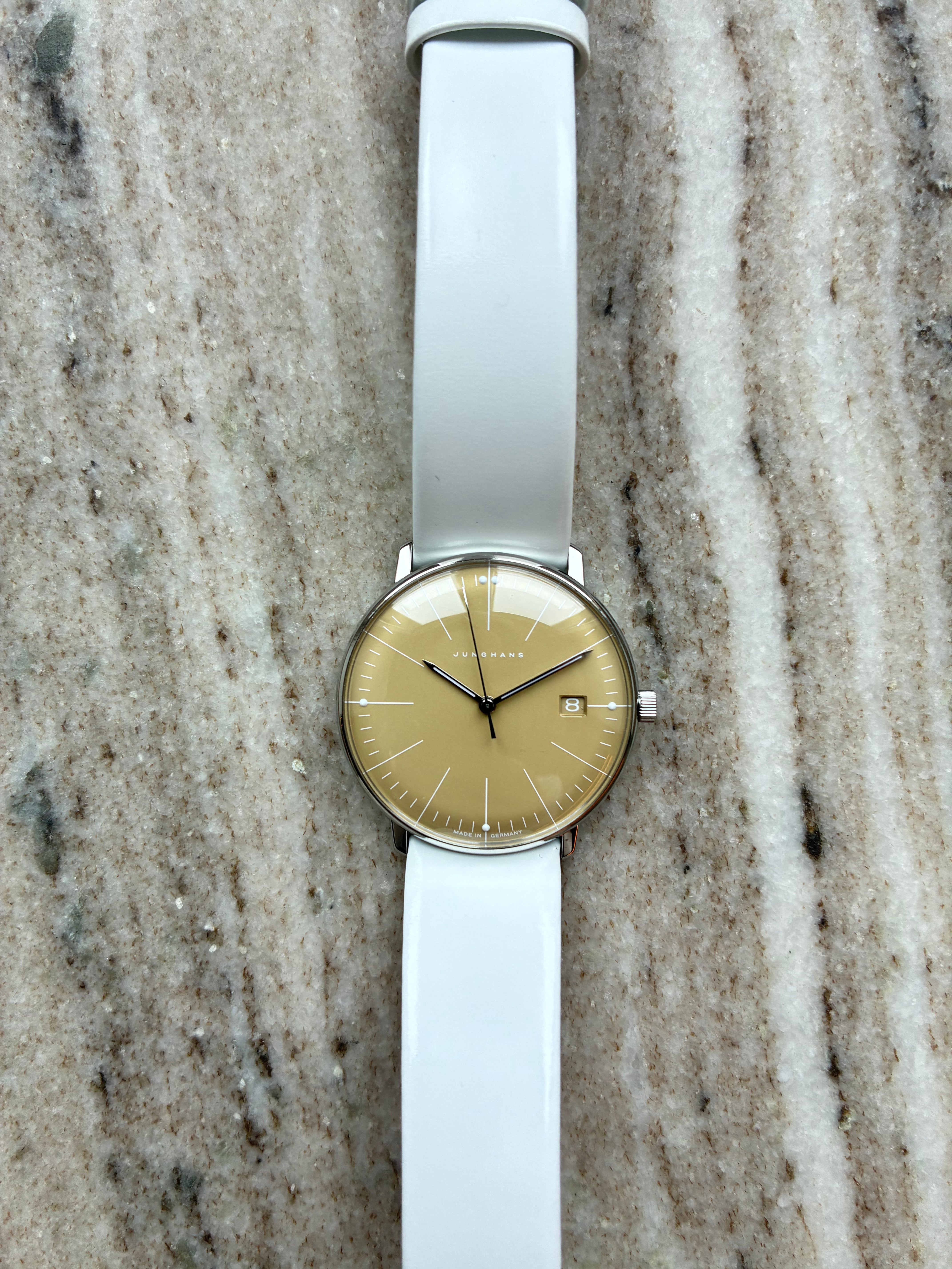 Junghans Max Bill Lady: Frontansicht einer Uhr mit goldenem Zifferblatt, weißem Lederarmband auf Marmor Hintergrund