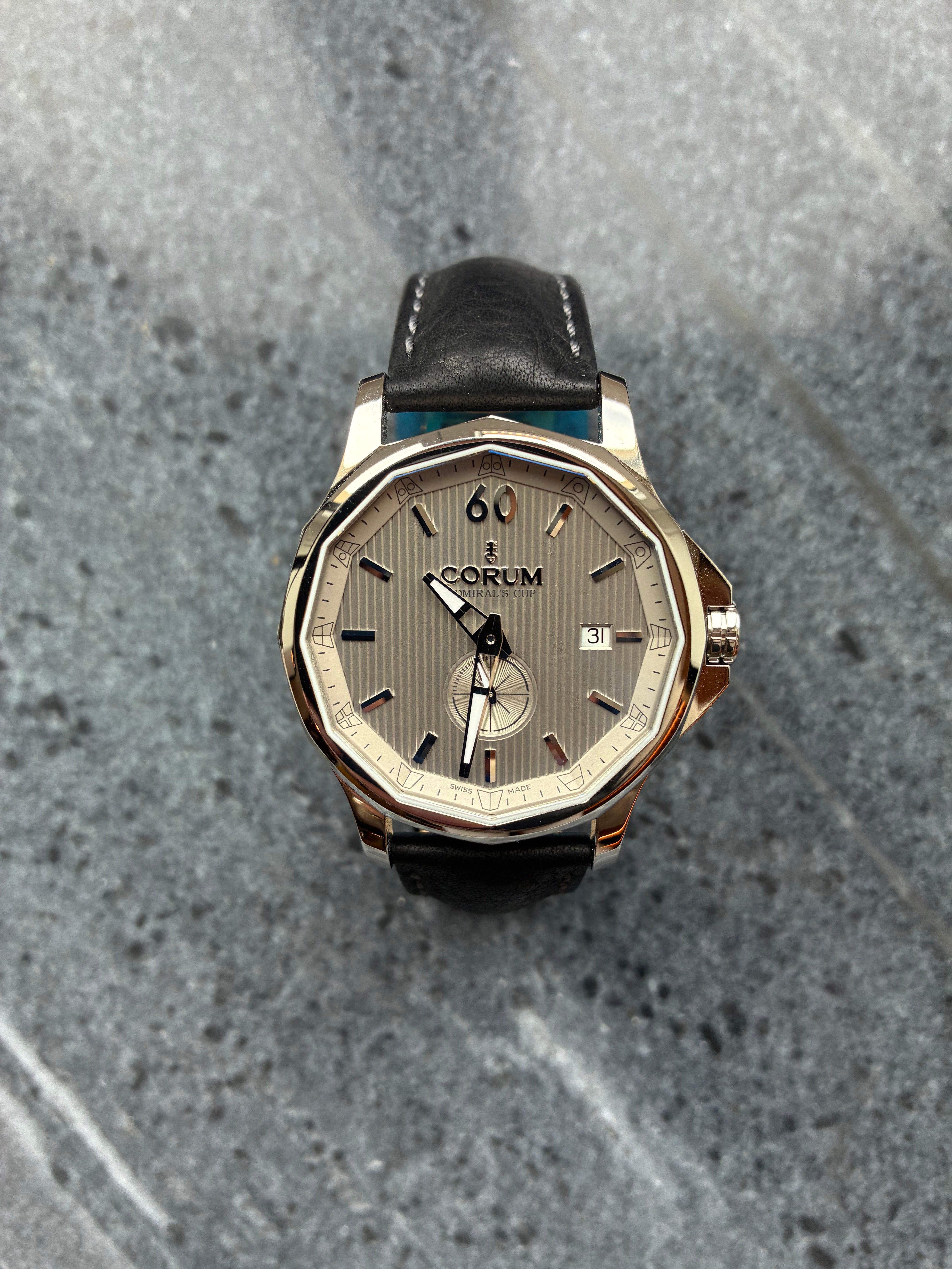 Corum Admiral's Cup Legend 42mm Automatik mit grauem Zifferblatt und schwarzem Lederarmband auf Steinhintergrund