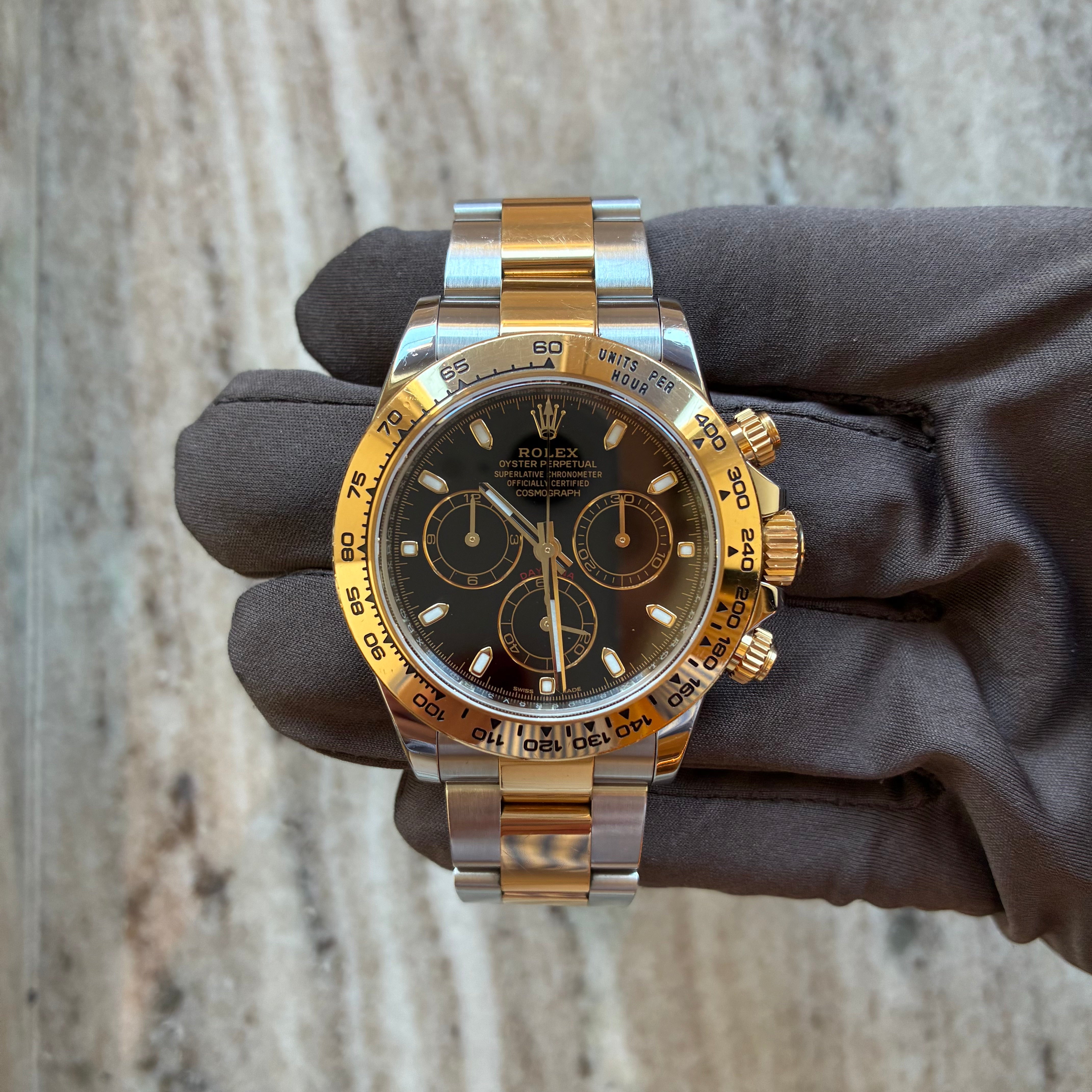 Rolex Daytona Bicolor 2016 mit schwarzem Zifferblatt und Goldrand wird von einer Hand mit grauer Handschuh getragen
