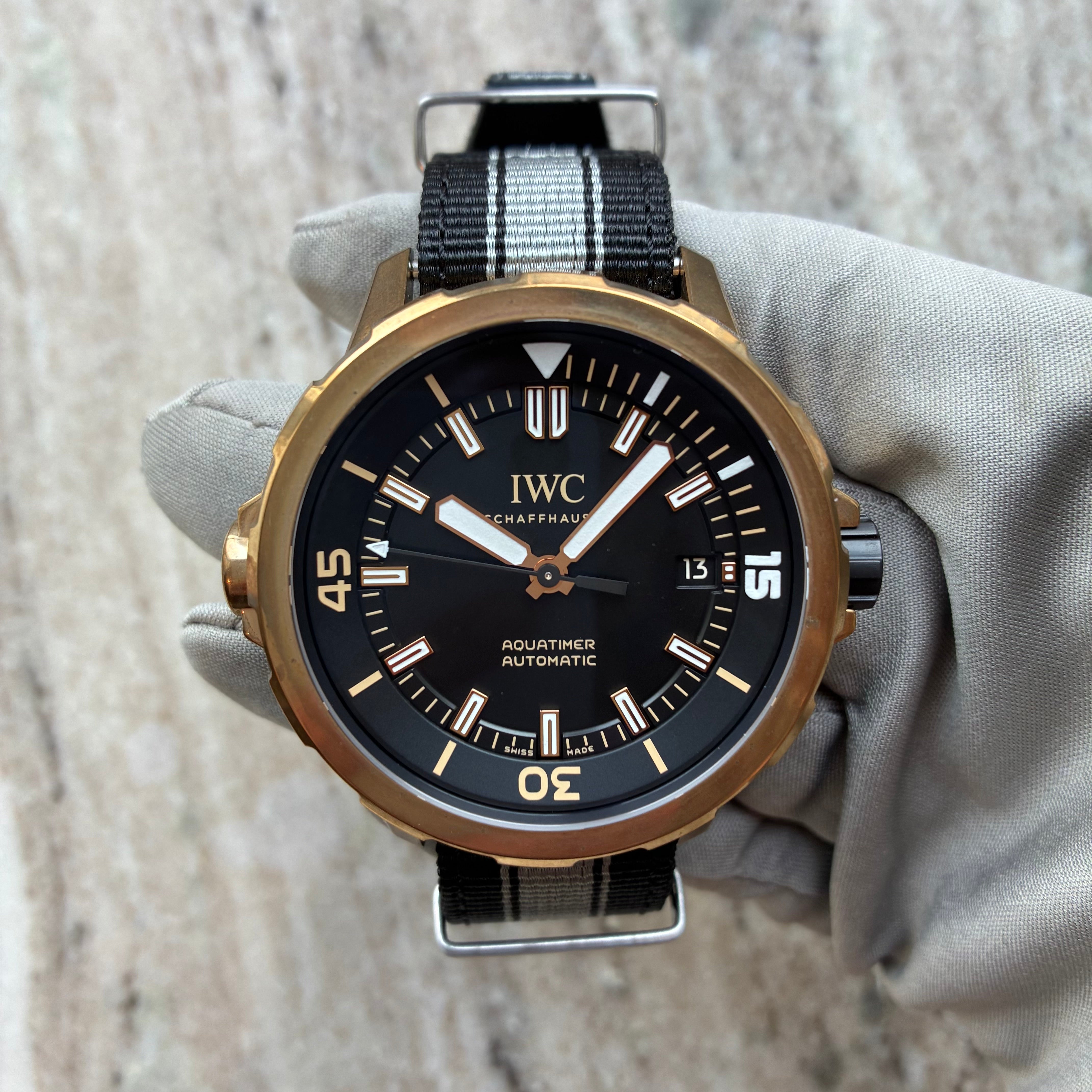 IWC Aquatimer Automatic in Bronze, gehalten in einer Hand mit grauem Handschuh, schwarzes Zifferblatt, Nato-Armband