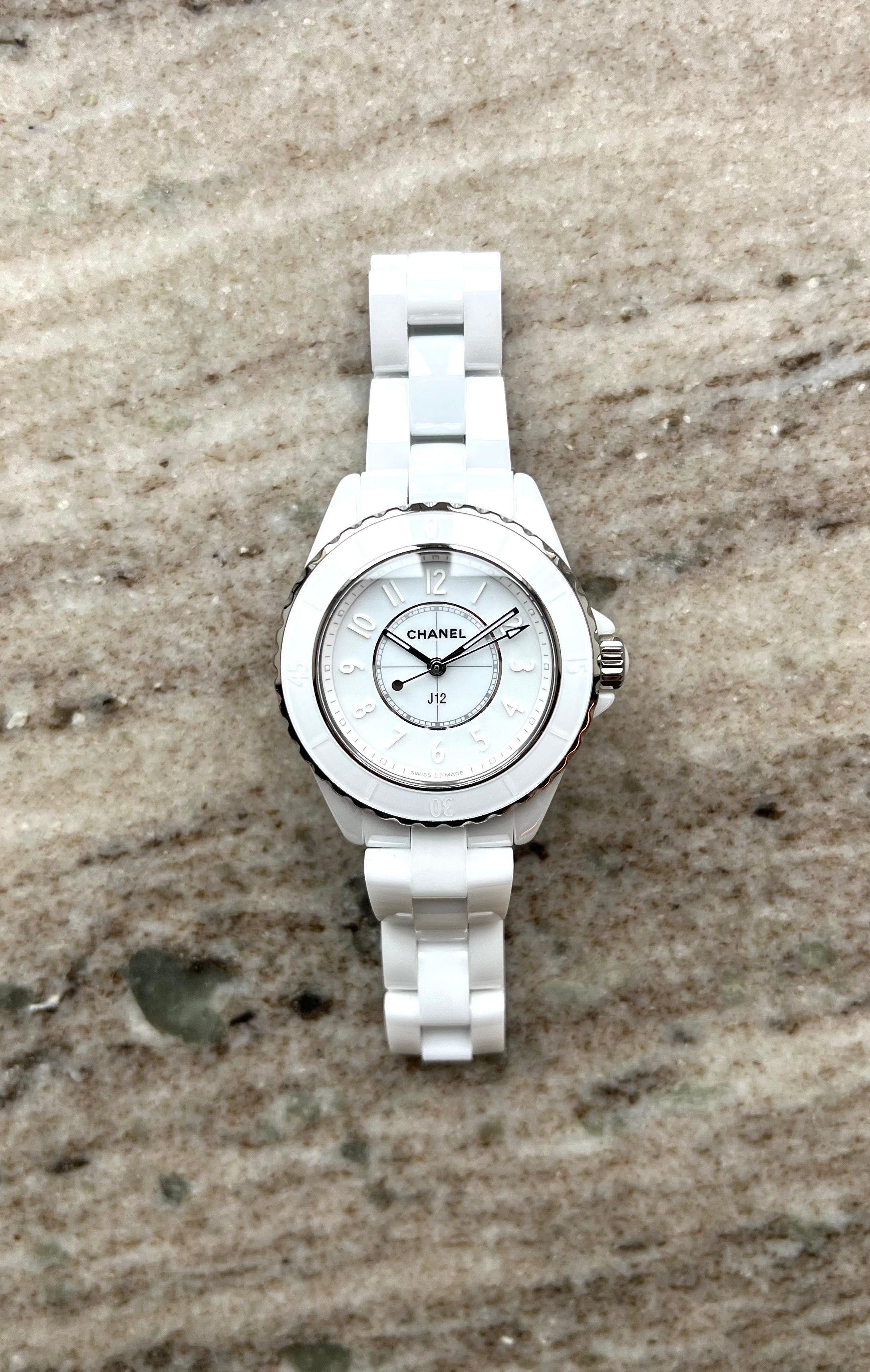 Eine weiße Chanel J12 33mm Keramikuhr mit Quarzwerk liegt auf einem Steinuntergrund