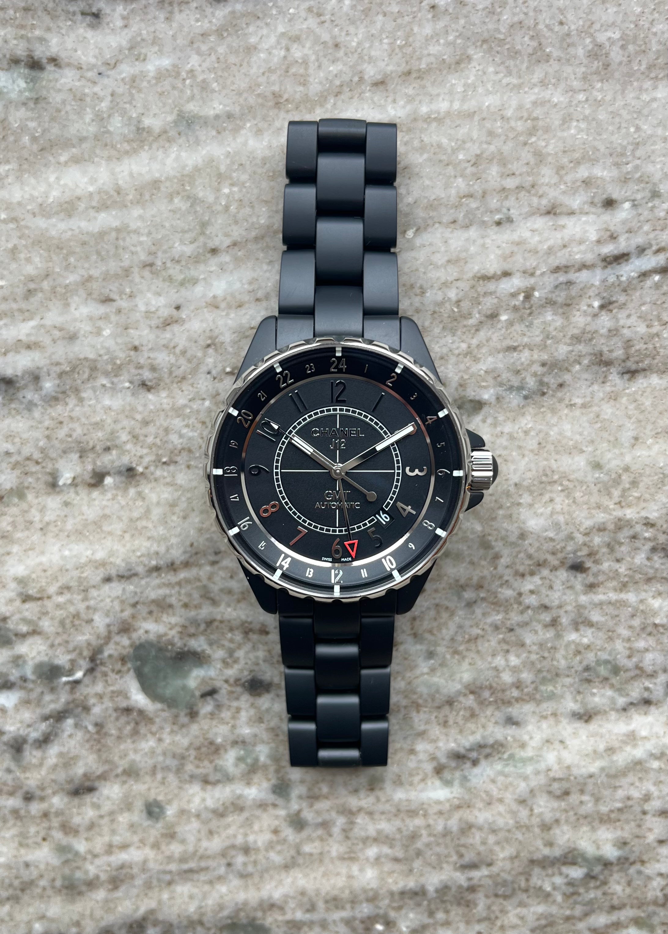 Chanel J12 GMT Keramik matt schwarz mit Automatikwerk und schwarzem Armband auf Marmor Hintergrund