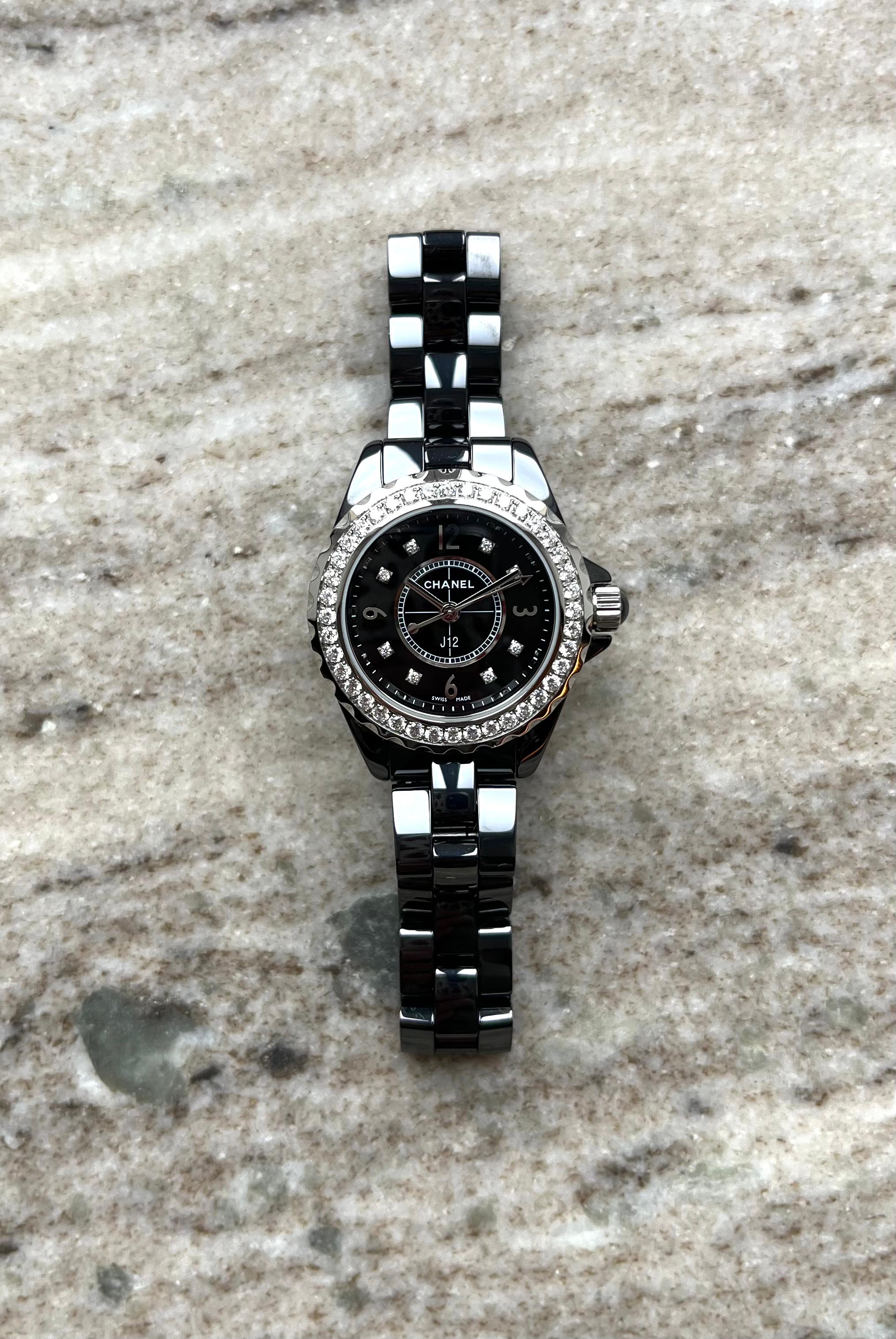 Chanel J12 29mm mit Diamanten besetzter Lünette und schwarzem Keramikarmband auf Steinuntergrund