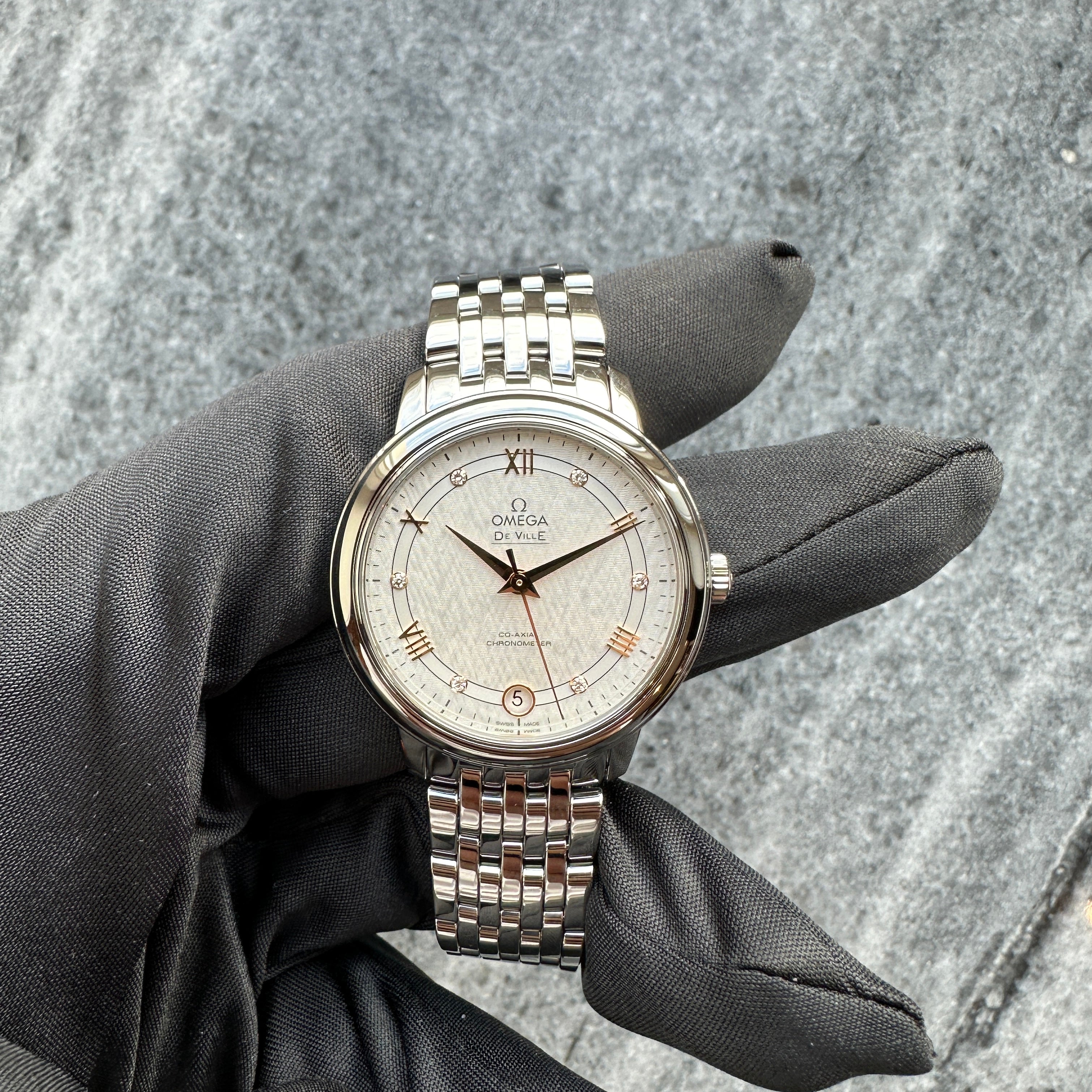 Omega De Ville Prestige Lady mit silbernem Zifferblatt und Stahlarmband auf grauem Hintergrund