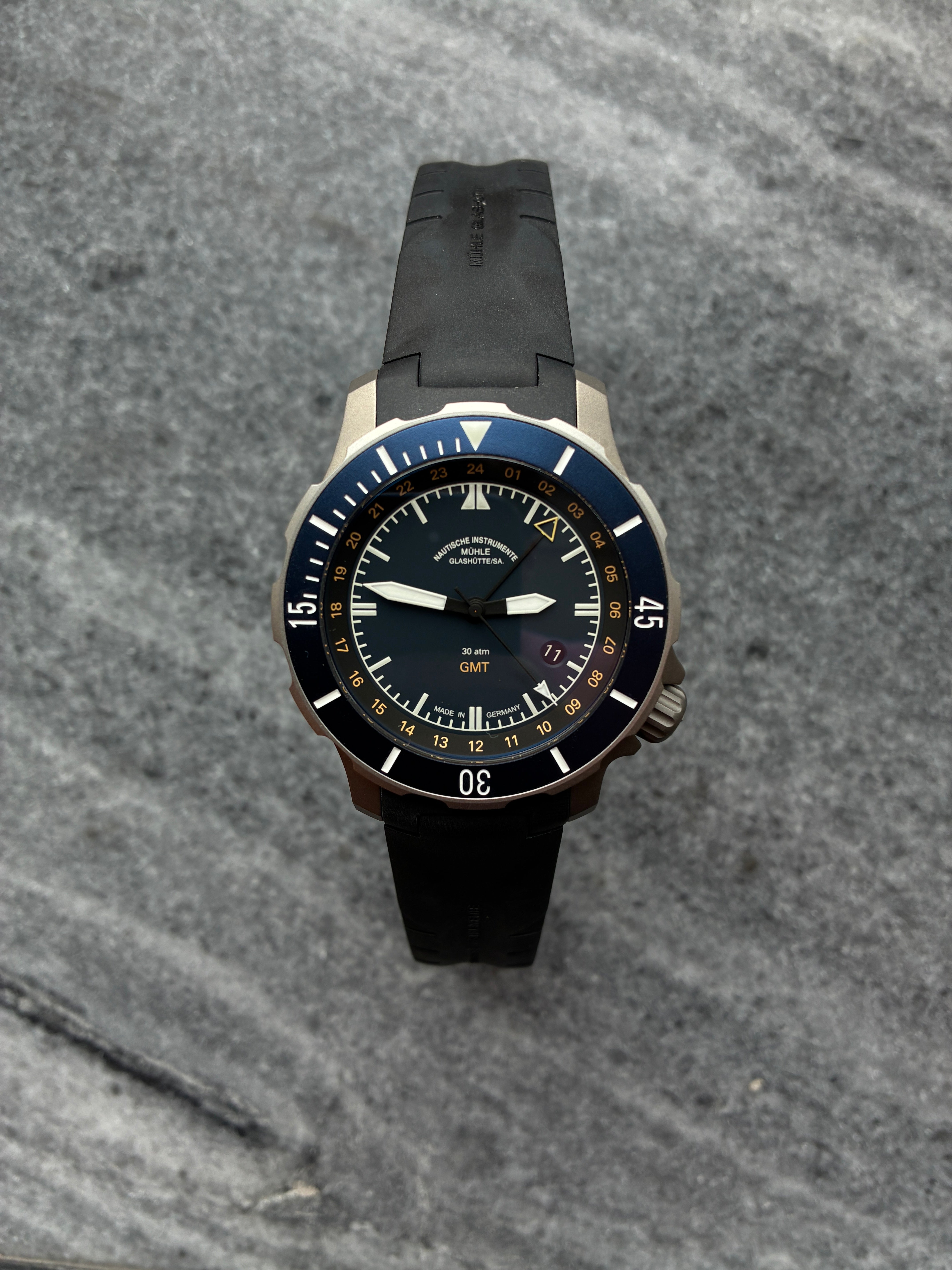 Mühle Glashütte Seebataillon GMT mit blauem Zifferblatt und schwarzem Kautschukband auf grauem Hintergrund