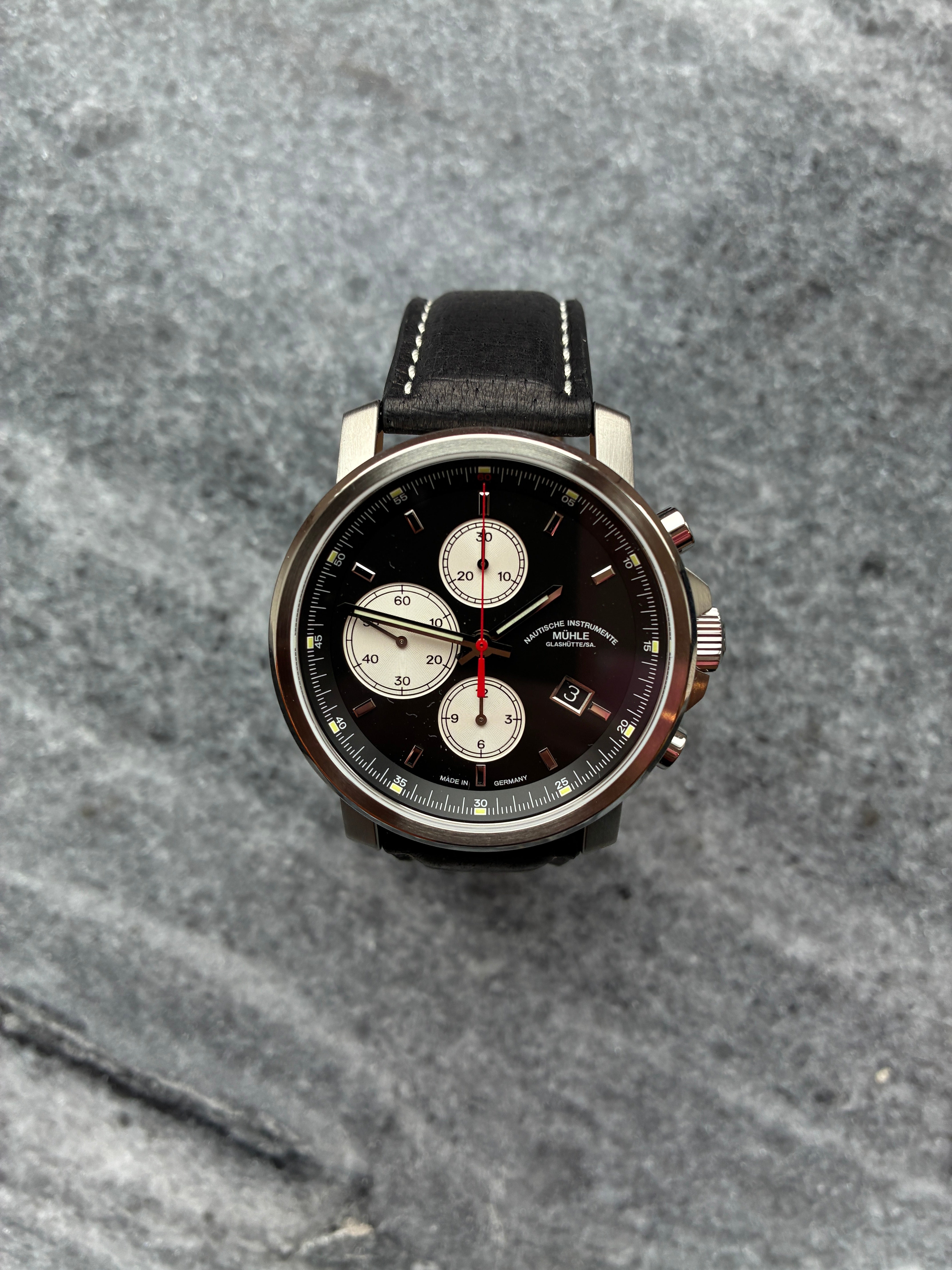 Mühle Glashütte 29er Chronograph mit schwarzem Zifferblatt und schwarzem Lederarmband auf Steinuntergrund