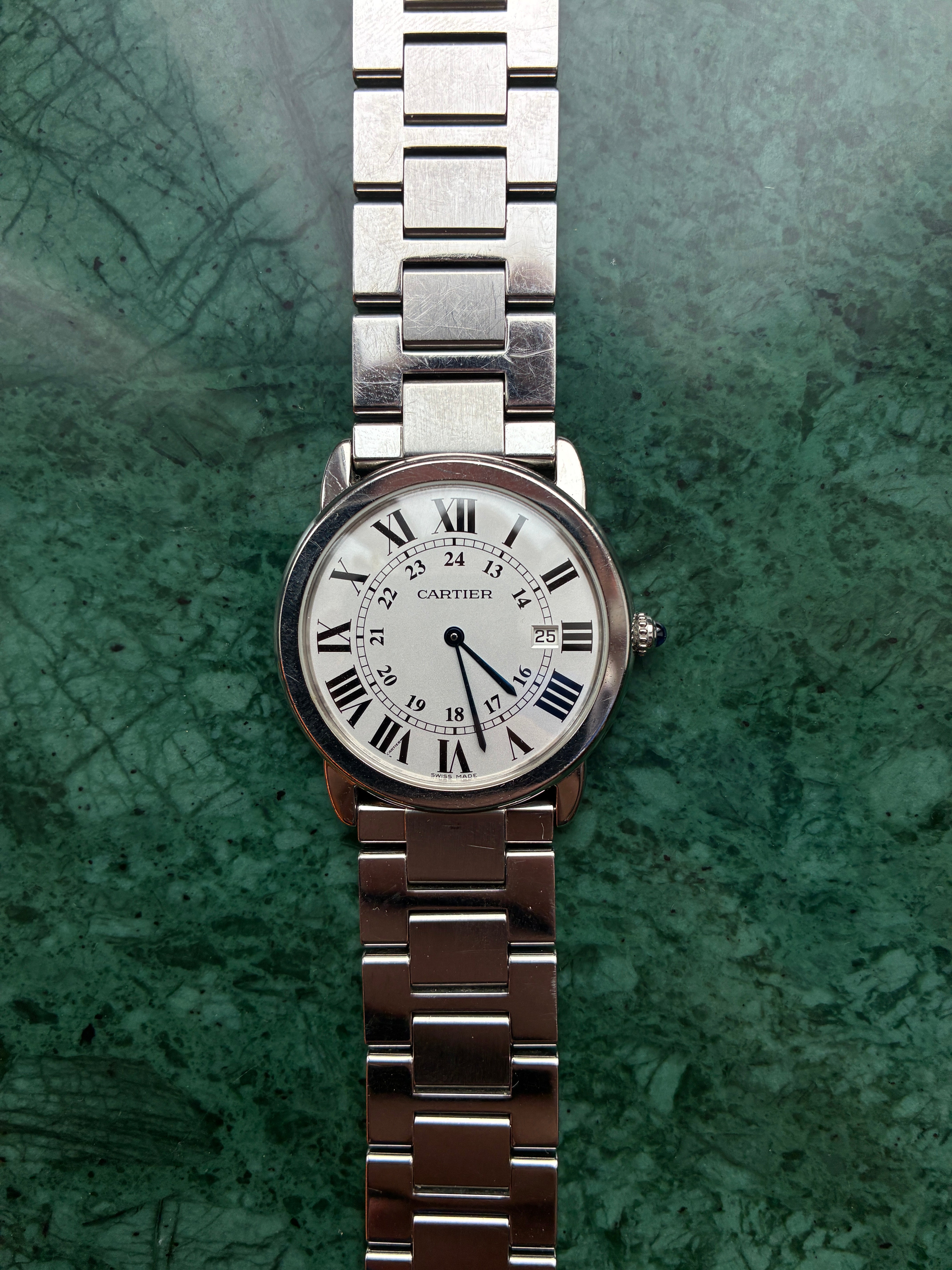 Cartier Ronde Solo de Cartier Quarz Damenuhr aus Edelstahl mit weißem Zifferblatt und silbernem Armband auf grünem Hinterg…