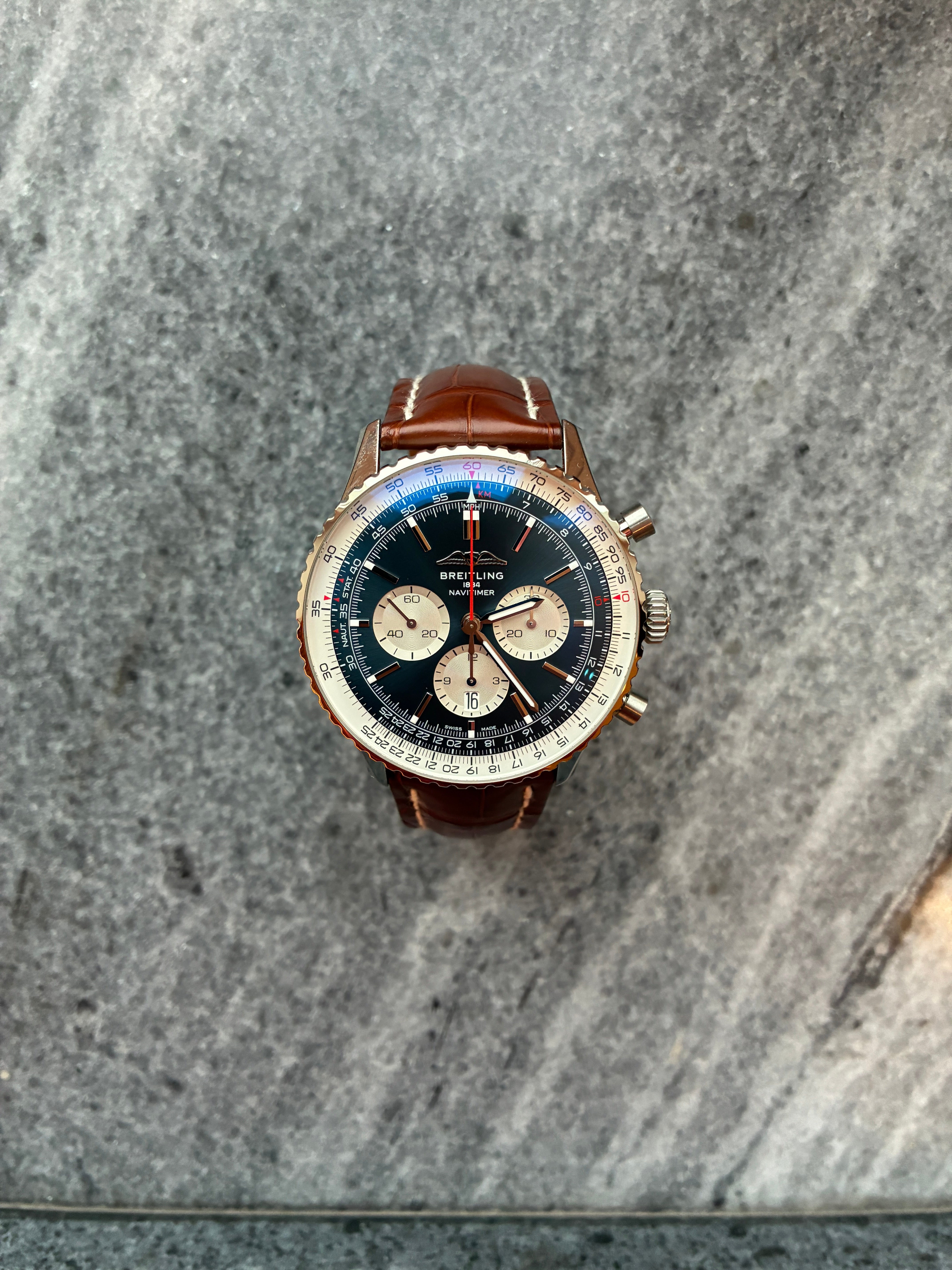 Breitling Navitimer B01 Chronograph 46 mit blauem Zifferblatt und braunem Lederarmband auf grauem Stein