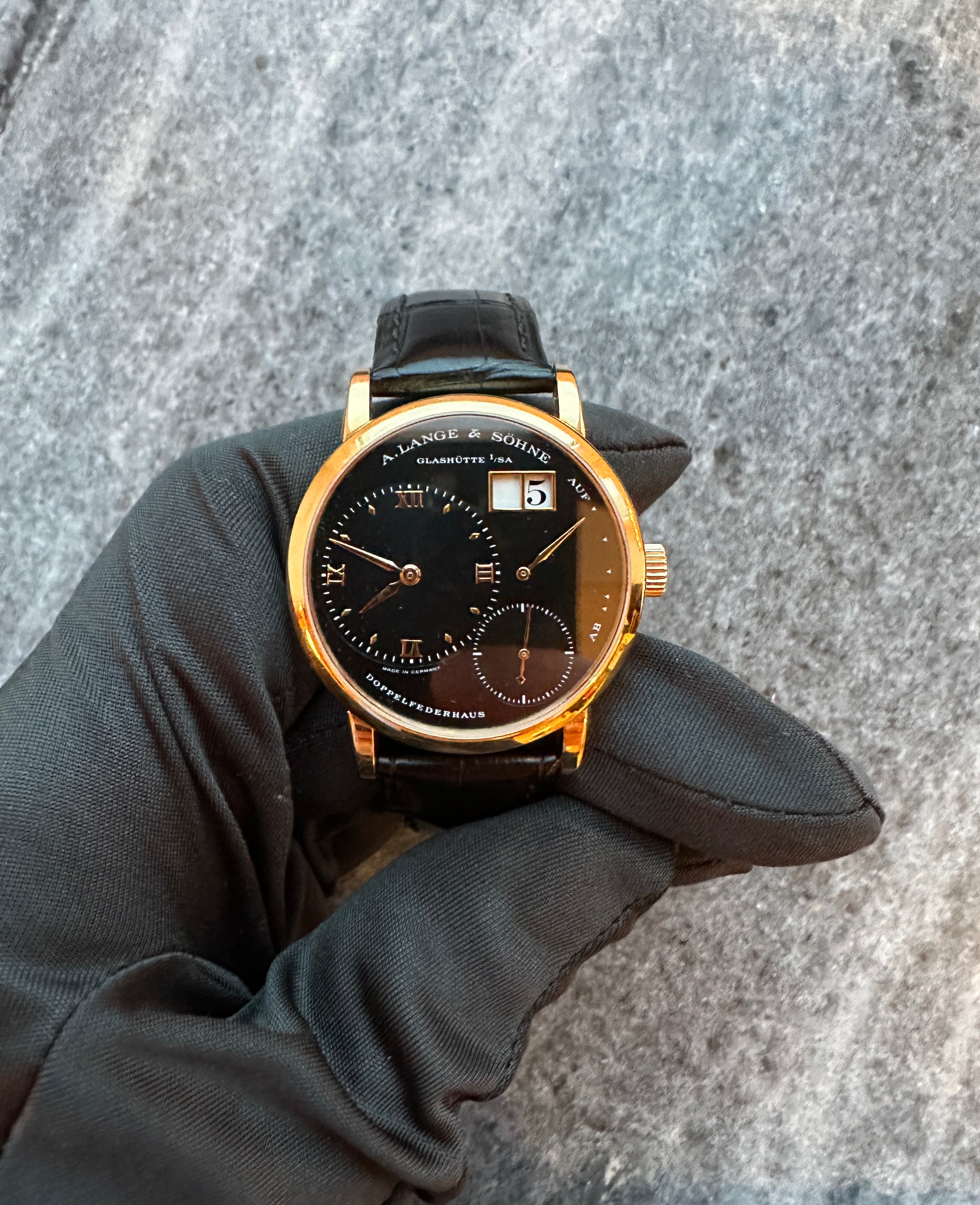 A. Lange & Söhne Kleine Lange 1 mit schwarzem Zifferblatt in Goldgehäuse, auf Stoffuntergrund