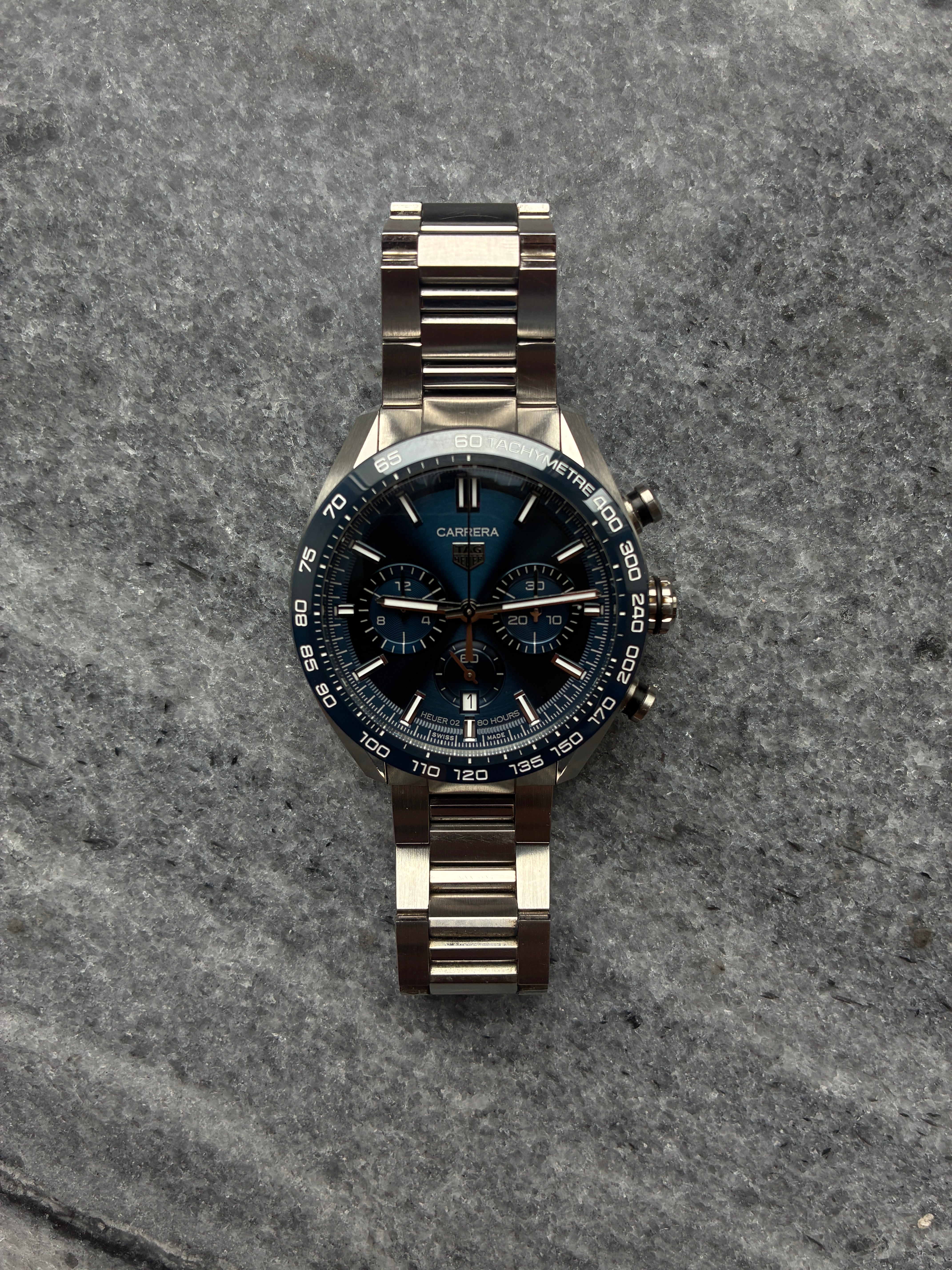 Tag Heuer Carrera Chronograph mit blauem Zifferblatt und Stahlband auf grauem Steinuntergrund
