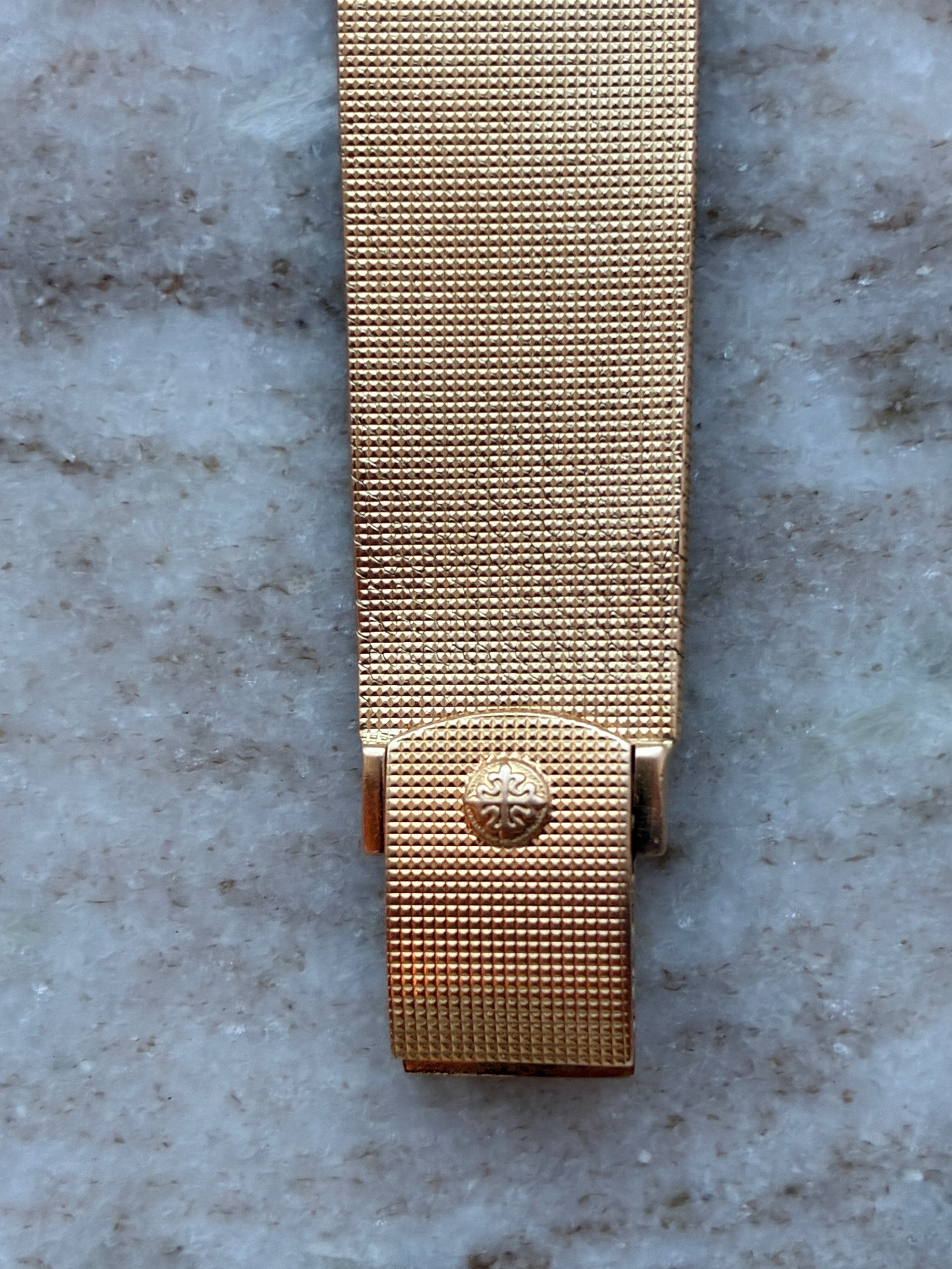 Patek Philippe Ellipse d'Or Service 2025 goldenes Armband und Schließe mit Logo auf Marmoruntergrund