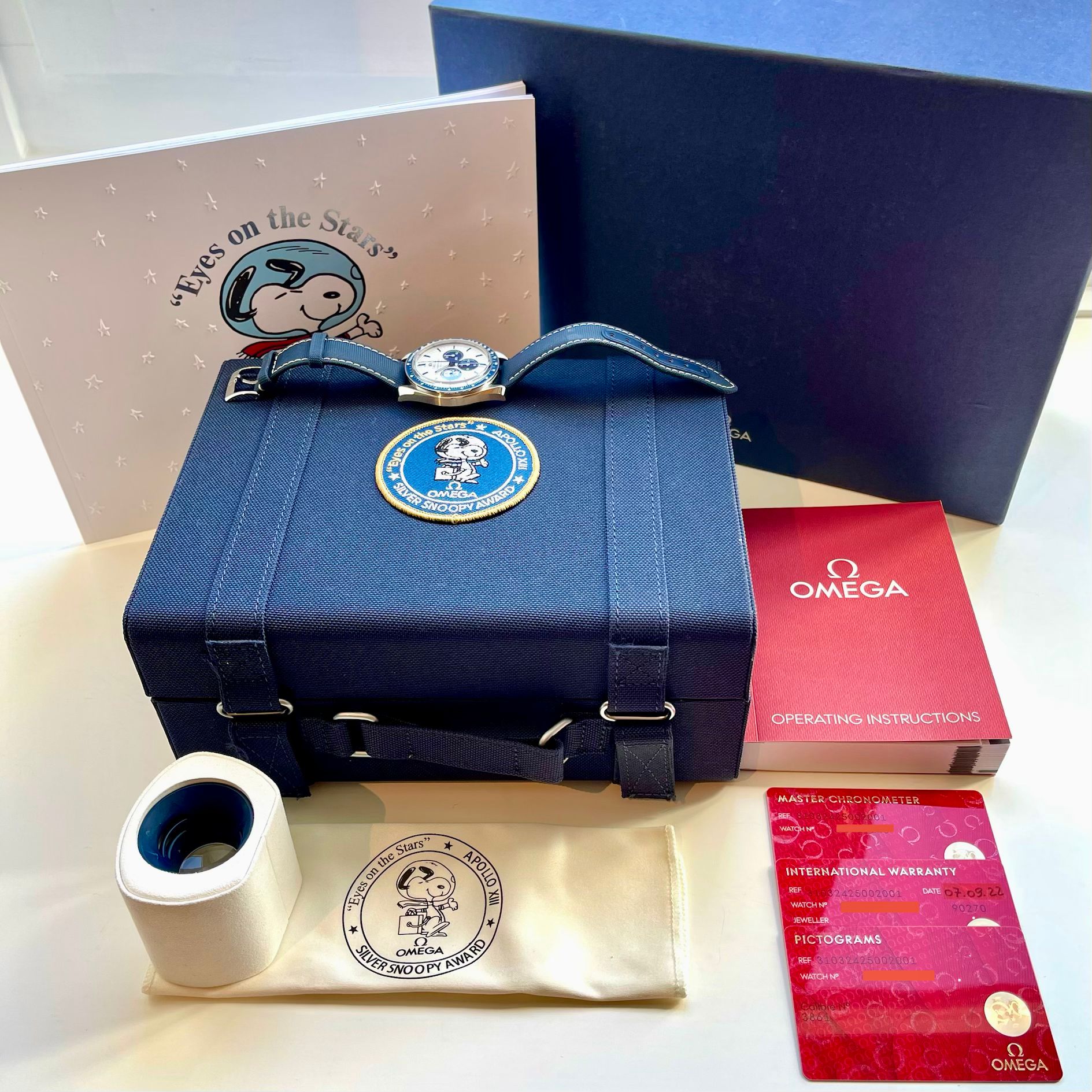 Die Omega Speedmaster "Silver Snoopy Award" 50th Anniversary (2022) in voller Verpackung mit allen Dokumenten auf hellem Hintergrund